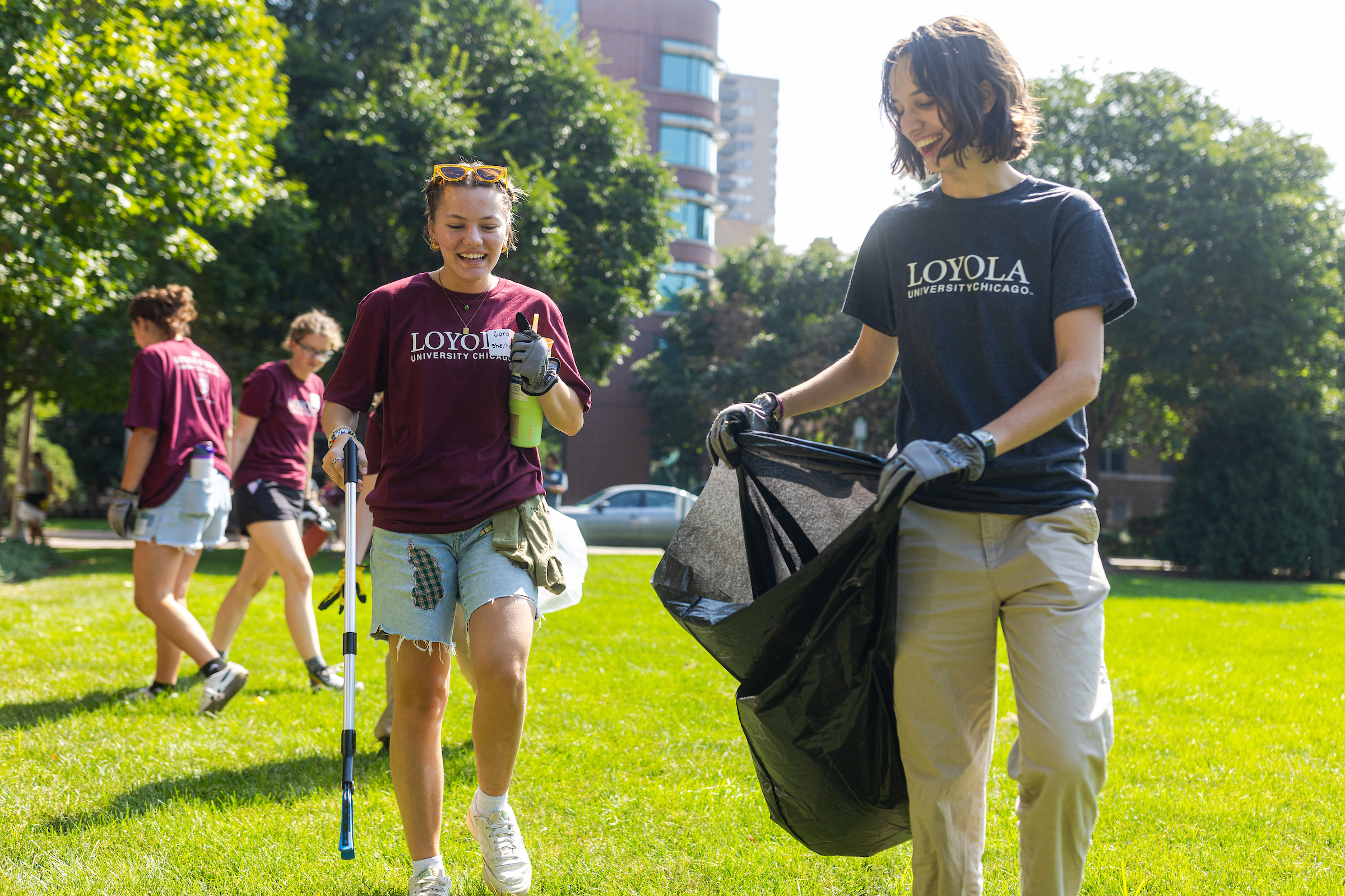 Two Loyola Students picking up trash and carry a trash bag while smiling